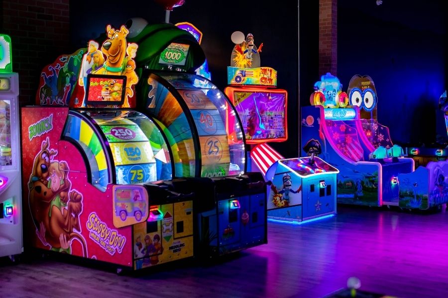 A vibrant arcade room at The Rush Funplex filled with various arcade games and colorful lighting.