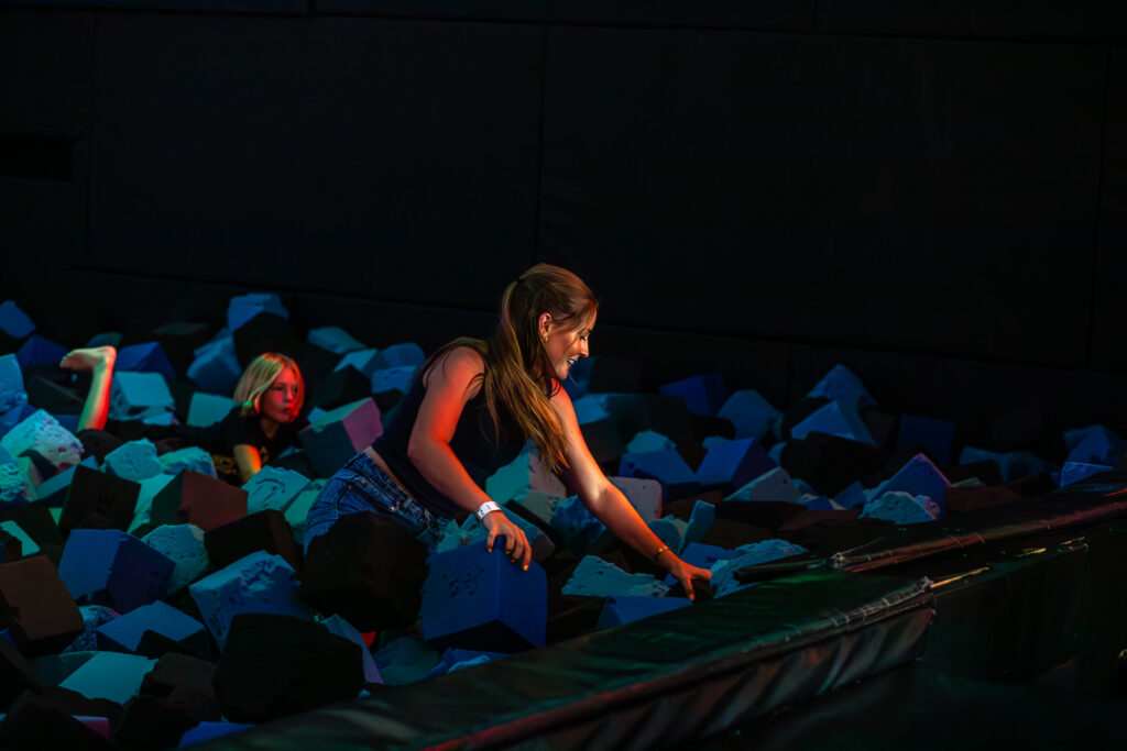 A woman jumps on a trampoline in a dark room at The Rush Funplex, showcasing her excitement and energy.