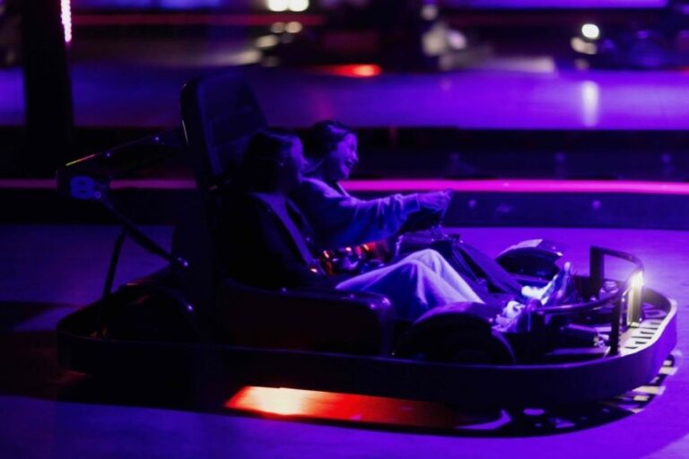 Two people racing in go-karts at night at The Rush Funplex, illuminated by colorful lights and a vibrant atmosphere.