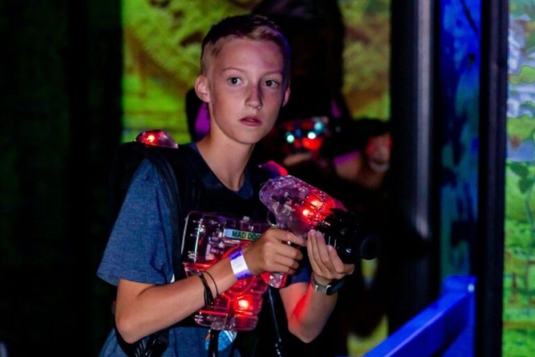 A young boy stands with a toy gun in front of a screen at The Rush Funplex, enjoying an interactive gaming session.